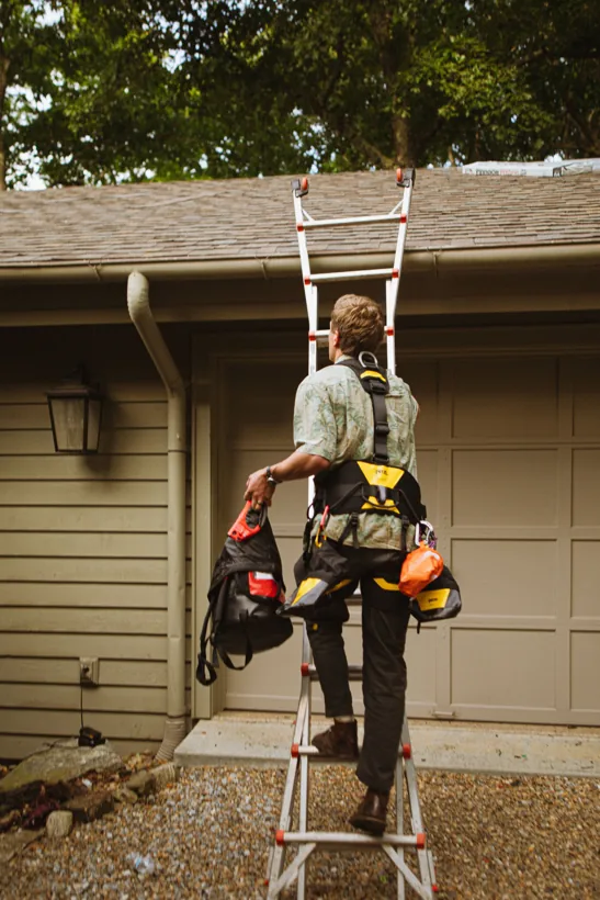 Roofer with safety gear climbing a ladder